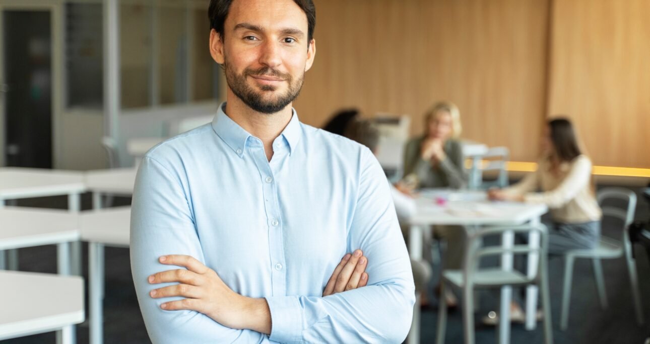 Confident smiling salesman with crossed arms working in modern office