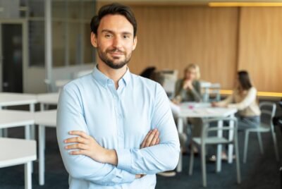 Confident smiling salesman with crossed arms working in modern office